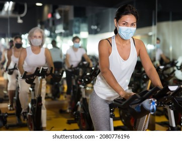 Asian Female In Face Mask With Fitness Bike During Cycling Class In Modern Gym