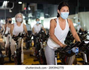 Asian Female In Face Mask With Fitness Bike During Cycling Class In Modern Gym