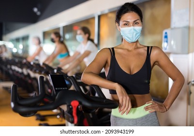 Asian Female In Face Mask With Fitness Bike During Cycling Class In Modern Gym