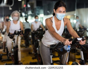 Asian Female In Face Mask With Fitness Bike During Cycling Class In Modern Gym