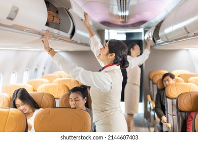 Asian female flight attendant closing the overhead luggage compartment lid for carry on baggage after passengers are seat and prepare to take off