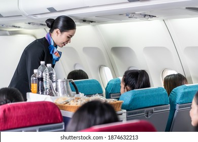 Asian Female Flight Attendant Serving Food And Drink To Passengers On Airplane. The Cabin Crew Pushing The Cart On Aisle To Serve The Customer. Airline Service Job And Occupation Concept.