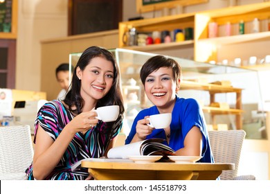 Asian Female Friends Enjoying Her Leisure Time In A Cafe, Drinking Coffee Or Cappuccino And Talking About Some Things