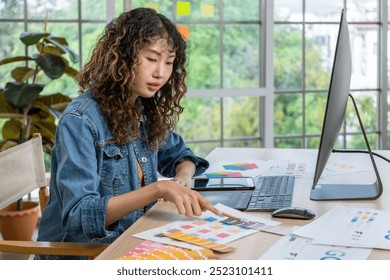 Asian female graphic designer reviewing color swatches while working on a creative design project in a modern office - Powered by Shutterstock