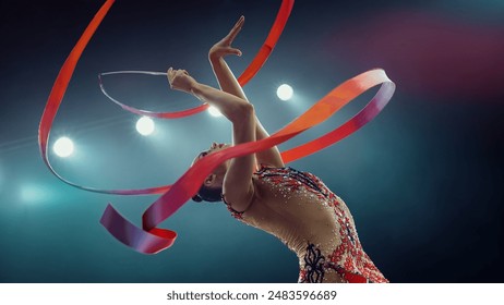 Asian Female Gymnast in Dazzling Costume, Gracefully Maneuvering Vibrant Ribbon Under Bright Stadium Lights, Her Artistic Flair and Precision in an Enthralling Gymnastics Performance. - Powered by Shutterstock