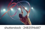 Asian Female Gymnast Elegantly Twirls Vibrant Ribbon Under Bright Stadium Lights, Her Precision, Grace, and Artistry in Captivating Rhythmic Gymnastics Performance.