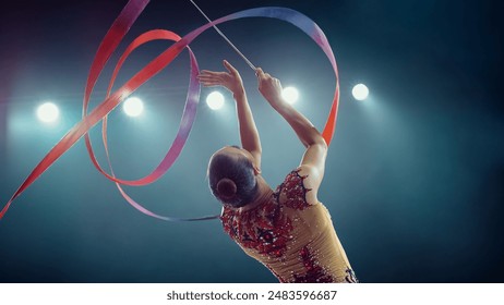 Asian Female Gymnast Elegantly Twirls Vibrant Ribbon Under Bright Stadium Lights, Her Precision, Grace, and Artistry in Captivating Rhythmic Gymnastics Performance.