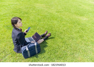 Asian Female High School Student Using A Laptop Pc And A Smart Phone On Grass Field.