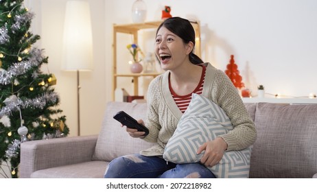 Asian Female Holding A Tv Controller Is Roaring And Booing With Hand Gestures While Relaxing By Binge Watching Hilarious Episode In The Christmas Atmosphere Home Interior.