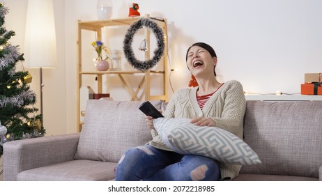 Asian Female Holding A Tv Controller Is Roaring And Booing With Hand Gestures While Relaxing By Binge Watching Hilarious Episode In The Christmas Atmosphere Home Interior.