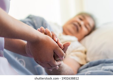 asiatische Hausfrauen, die die Hand einer älteren Frau auf dem Bett halten und die Patientin ermutigen