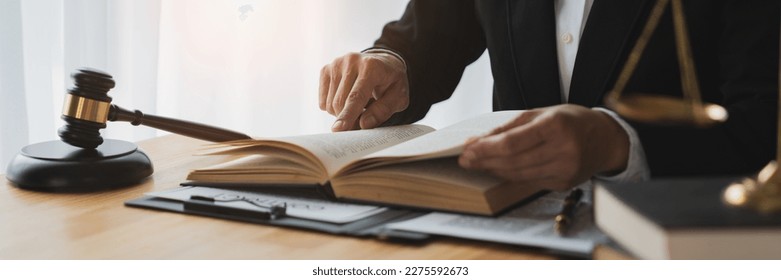 Asian female lawyer, law adviser, businesswoman sitting and reading with finger pointing at legal code information. Business agreement on book working with scales and hammer in office. - Powered by Shutterstock
