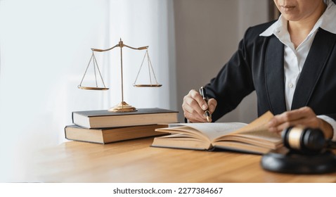 Asian female lawyer or legal advisor working on the scale of justice sitting at her desk and holding a pen to look at the information Detailed content about the scale of jurisprudence to study. - Powered by Shutterstock