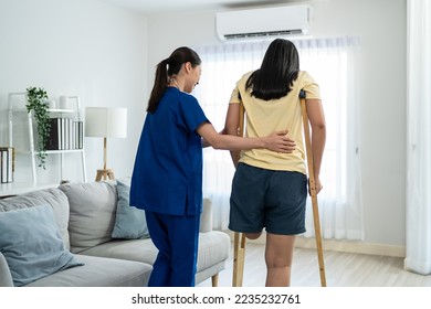 Asian female leg amputee doing physiotherapy with support from nurse. Attractive young girl legless patient practice walking slow with walker crutch with woman caregiver doctor in living room at home. - Shutterstock ID 2235232761