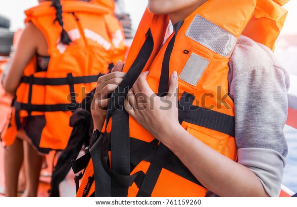 Asian female in life jacket with other people near
sea on ship