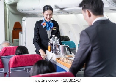 Asian female and male flight attendant serving food and drink to passengers on airplane. The cabin crew pushing the cart on aisle to serve the customer. Airline service job and occupation concept.