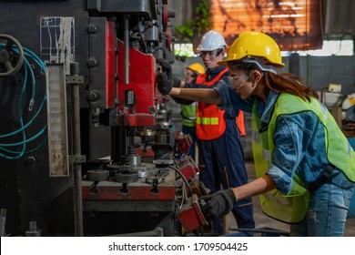 asian female and male manufacturing workers operating steel drilling machine together in line of metal work production factory