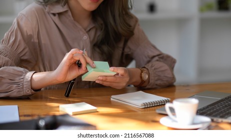 Asian Female Marketing Officer Taking Her Creative Ideas On Memo Pad Sticky Notes At Her Office Desk.