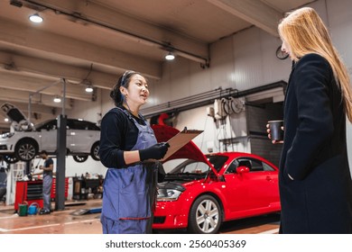 Asian female mechanic holding clipboard and explaining car repair to female customer in auto repair shop - Powered by Shutterstock