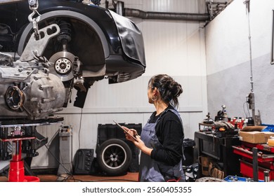 Asian female mechanic holding digital tablet and inspecting lifted car in auto repair shop - Powered by Shutterstock