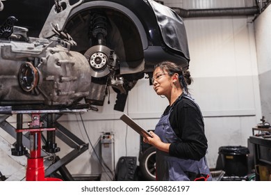 Asian female mechanic using a digital tablet and inspecting a car in a professional auto repair shop - Powered by Shutterstock