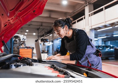 Asian female mechanic using a laptop for diagnostics while working on a car engine in a professional garage - Powered by Shutterstock