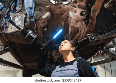 Asian female mechanic using a uv light inspecting the undercarriage of a car lifted on a hydraulic ramp in a modern vehicle repair shop - Powered by Shutterstock