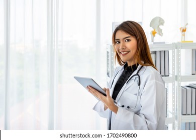 Asian female medical doctor using digital tablet in office clinic hospital with smiling and looking at camera