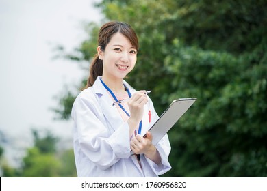 Asian Female Medical Worker In White Coat With Medical Chart And Pen