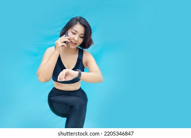 Asian Female Model Shows Off Her Exercise Habits While Talking On Her Cell Phone And Checking Her Health Through A Digital Watch.(include Path On Isolated Background)