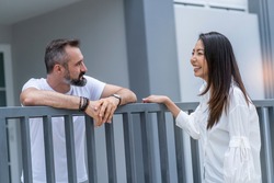 An Asian Female Neighbor Walks To Say Hello To A Male Neighbor In Front Of The Fence. 