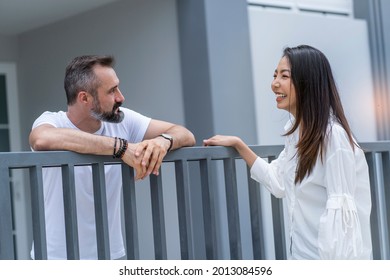 An Asian female neighbor walks to say hello to a male neighbor in front of the fence. 