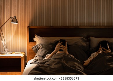 Asian female with nomophobia,excessive use of cell phone,addicted to social media,lying on bed looking at mobile phone screen in bedroom at night before bedtime,smartphone syndrome,Nomophobia concept