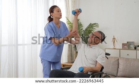 asian female nurse assisting disabled grandfather on wheelchair while he is holding up dumbbells for rehab training at home. domiciliary care for senior people concept