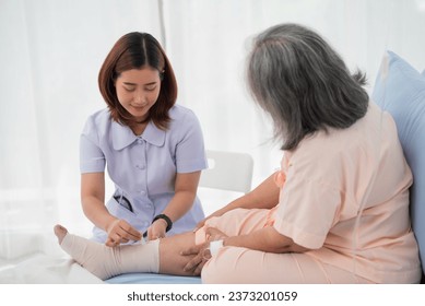 Asian female nurse bandaging foot of elderly woman patient at the hospital - Powered by Shutterstock