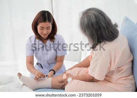 Asian female nurse bandaging foot of elderly woman patient at the hospital