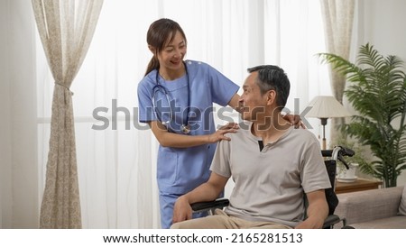 Asian female nurse and male senior wheelchair user enjoying chatting by the window at home. in-home social care for elderly disabled people concept