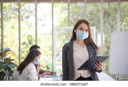 Asian female office worker wears hygienic mask on her face at work to protect from coronavirus or Covid-19. Concept for New normal lifestyle at work. Awareness of wearing facemask.Soft focus - Powered by Shutterstock