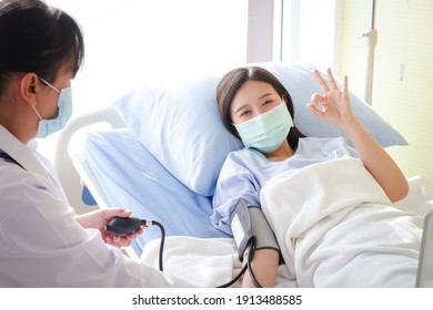 Asian Female Patients Wear A Blue Mask And Lie On A Hospital Bed. Raise Your Hand. Okay. The Doctor Measures The Patient's Pressure. Concept Of Medical Service, Health Insurance