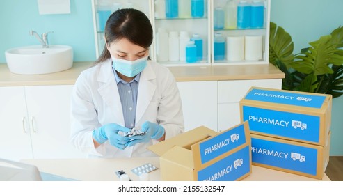 Asian Female Pharmacist Wear Mask And Surgical Glove Checking Packing Medication Into Package Box In Pharmacy For Delivery Service