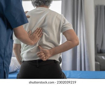 Asian female physiotherapist doing elderly asian gray haired female patient chiropractic pain treatment after having back pain and acute spine at clinic.