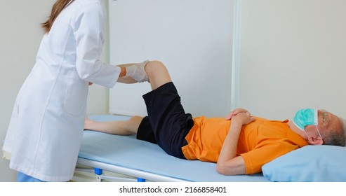 Asian Female Physiotherapist Is Helping Senior Elder Man Stretching His Hamstring And Doing Thigh Or Leg Rehabilitation In Exercise Room - He Lying On Massage Bed