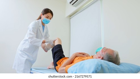 Asian Female Physiotherapist Is Helping Senior Elder Man Stretching His Hamstring And Doing Thigh Or Leg Rehabilitation In Exercise Room - He Lying On Massage Bed