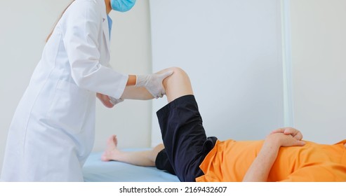 Asian Female Physiotherapist Is Helping Senior Elder Man Stretching His Hamstring And Doing Thigh Or Leg Rehabilitation In Exercise Room - He Lying On Massage Bed