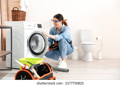 Asian female plumber fixing washing machine in bathroom - Shutterstock ID 2177750825