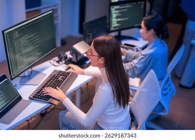 asian female programmer sits a dark tech workspace at night, fully focused on developing an online project. She writes HTML scripts and code for a modern website while contributing to automation work