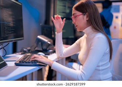 asian female programmer sits a dark tech workspace at night, fully focused on developing an online project. She writes HTML scripts and code for a modern website while contributing to automation work