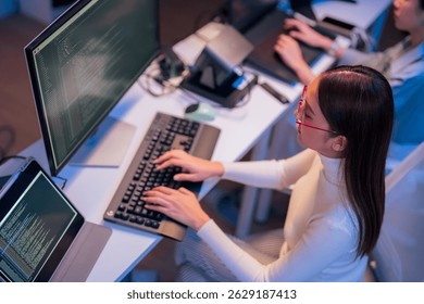 asian female programmer sits a dark tech workspace at night, fully focused on developing an online project. She writes HTML scripts and code for a modern website while contributing to automation work