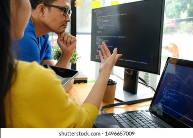 Asian female programmers wearing yellow shirts are pointing at their laptop screen for presentation to executives.
