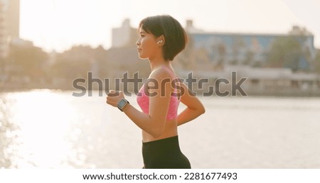 asian female runner wearing earbuds to listen music is jogging in city